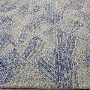 A textured rug displays blue, gray, and white interlocking triangular shapes on light wood flooring.