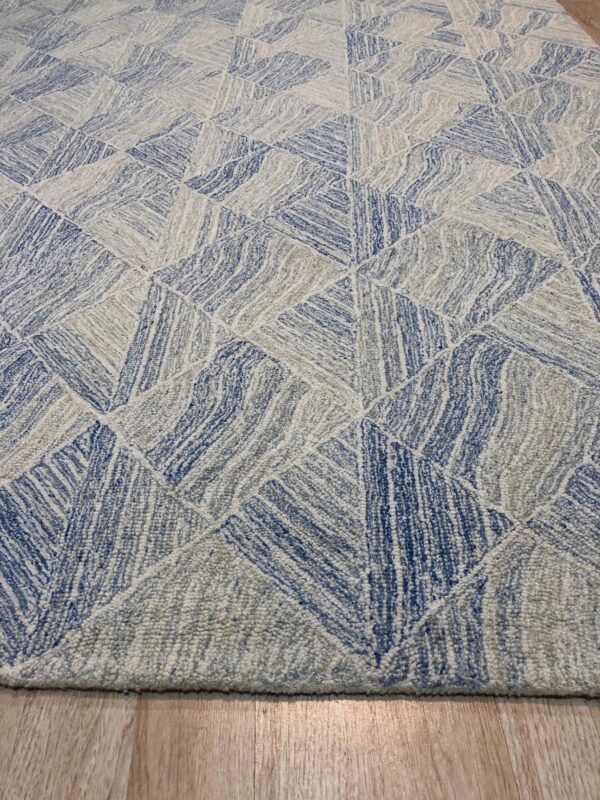 A textured rug displays blue, gray, and white interlocking triangular shapes on light wood flooring.
