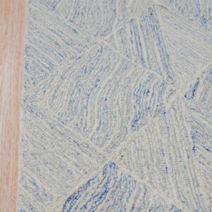 Textured light blue and white rug with an abstract linear pattern rests on light wood flooring.