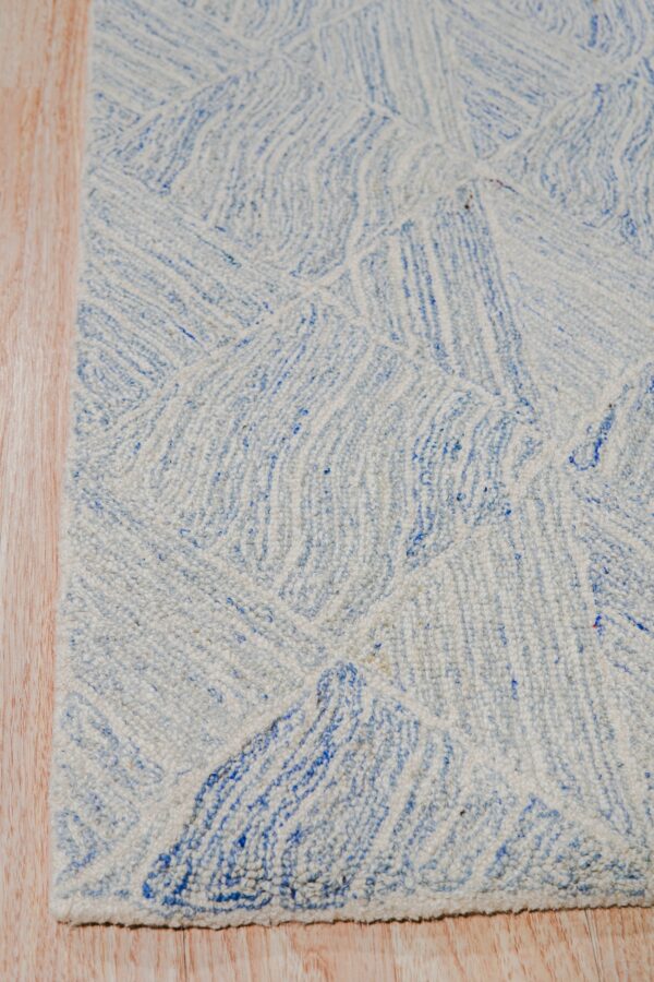 Textured light blue and white rug with an abstract linear pattern rests on light wood flooring.