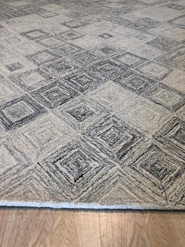 Textured gray and cream rug displaying a repeated diamond pattern sits on light wood flooring.