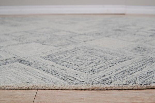 Close view of a chunky gray and cream rug featuring a geometric diamond pattern on wood flooring.