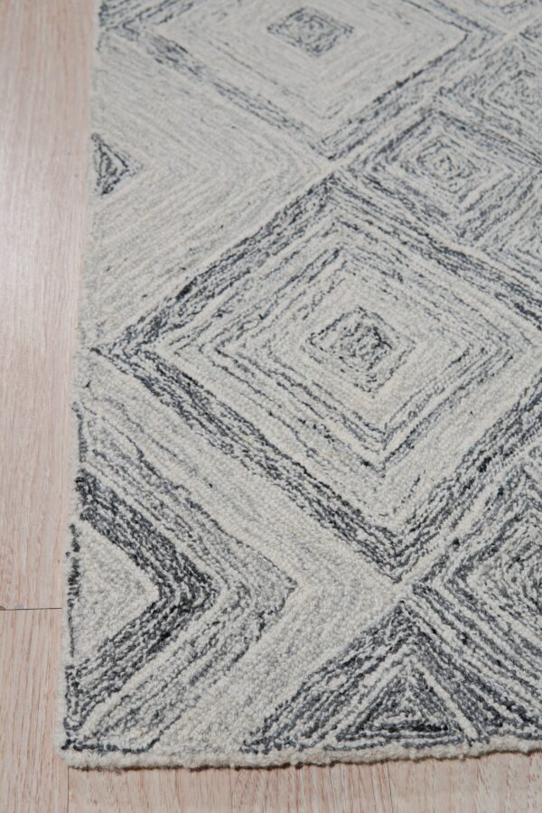 Textured white and dark gray rug featuring concentric diamond patterns rests on light wood plank flooring.