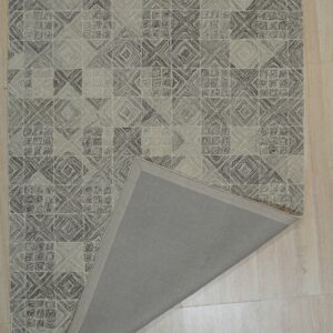 A beige and brown textured geometric rug lies on wood planks, folded back to show the plain gray backing.