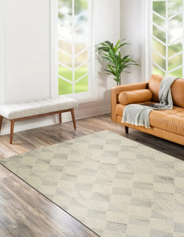 Off-white rug with a textured gray geometric block pattern rests on wood planks near a caramel leather sofa.