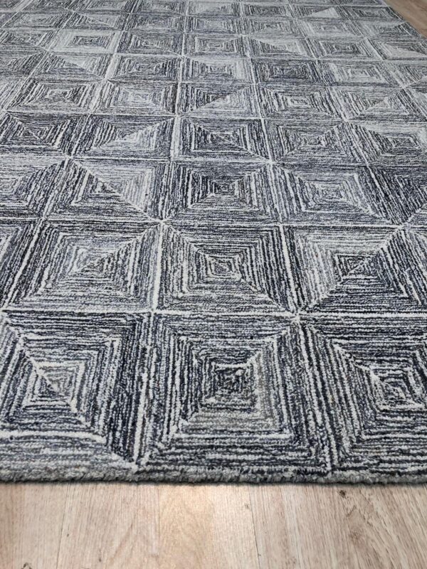 Textured gray and white rug featuring a repeating geometric pattern of concentric squares on wood flooring.