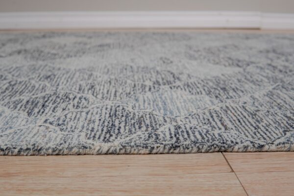 Textured blue and cream rug edge showing abstract pattern detail rests on light wood planks.