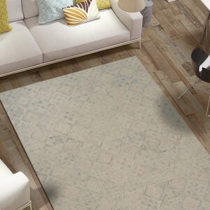 Beige rug with subtle blue and pink geometric patterns beneath a white sofa on distressed wood flooring.