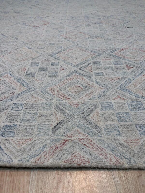 Textured off-white rug with geometric patterns in dusty blue and muted red, placed on light wood flooring.