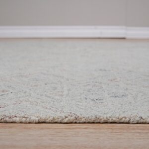 Textured off-white rug with colored flecks rests on light wood flooring near a white baseboard.
