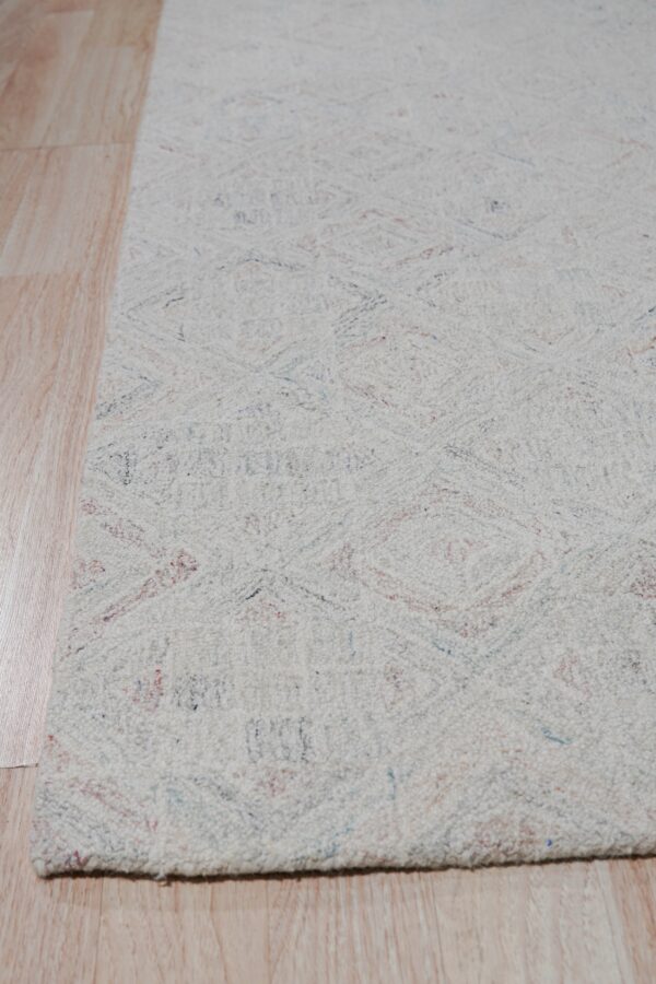 Off-white low-pile rug with faint multicolored geometric patterns rests on light hardwood planks.