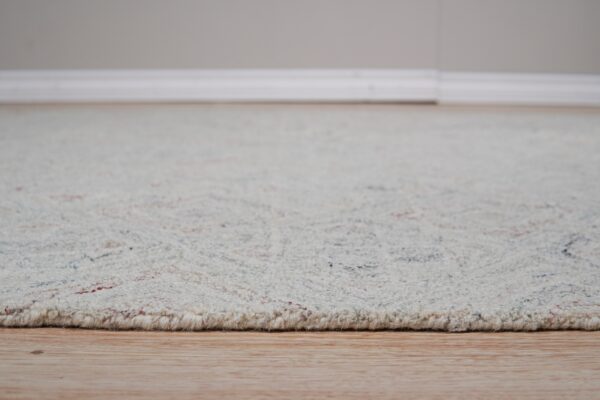 The textured, high pile edge of a speckled off-white rug rests on light wood flooring.