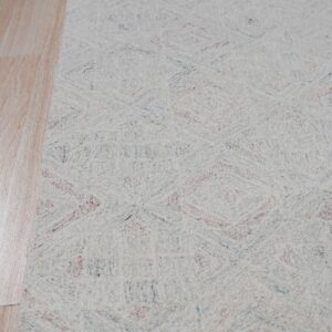 Light cream looped rug featuring a faint multicolored diamond pattern on wood flooring.