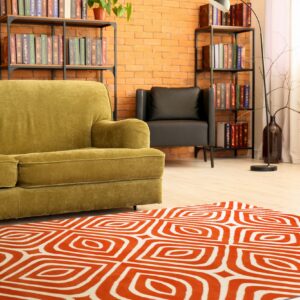Orange and white geometric rug on light wood flooring in a living room with an olive green sofa.