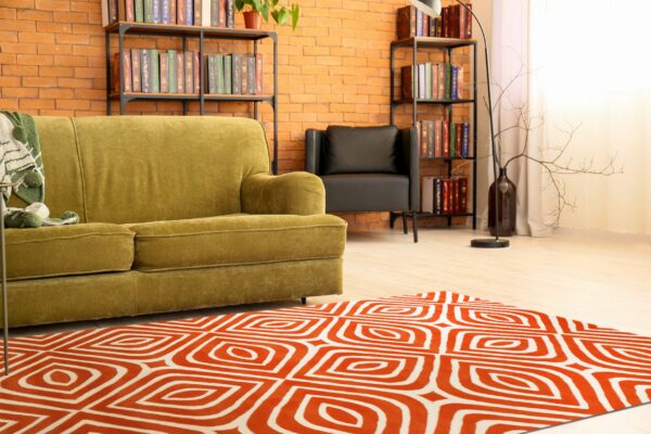Orange and white geometric rug on light wood flooring in a living room with an olive green sofa.