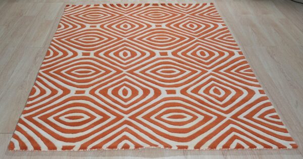 Orange and cream rug with a sculpted, repeating diamond geometric pattern rests on light wood flooring.