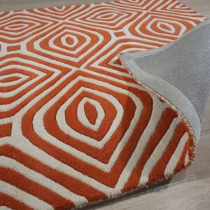 Close-up of a high-pile orange and cream geometric rug showing the woven gray backing on light flooring.