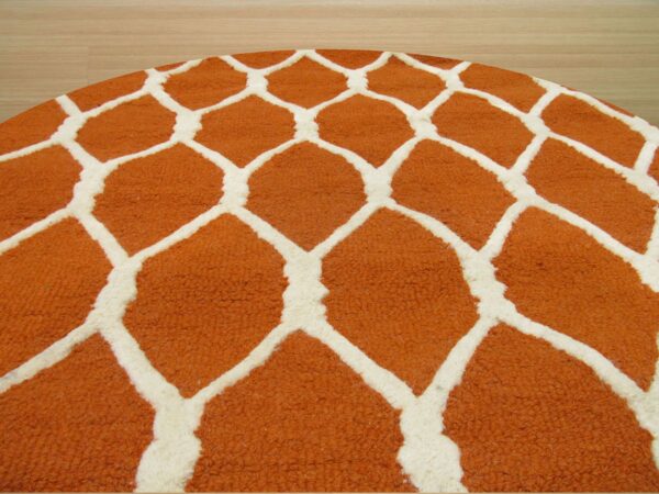 Round rug corner showing a textured rust and cream honeycomb pattern on light wood flooring.