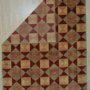 Red, sage, and tan geometric rug with repeating squares and triangles, displayed on light wood floor.