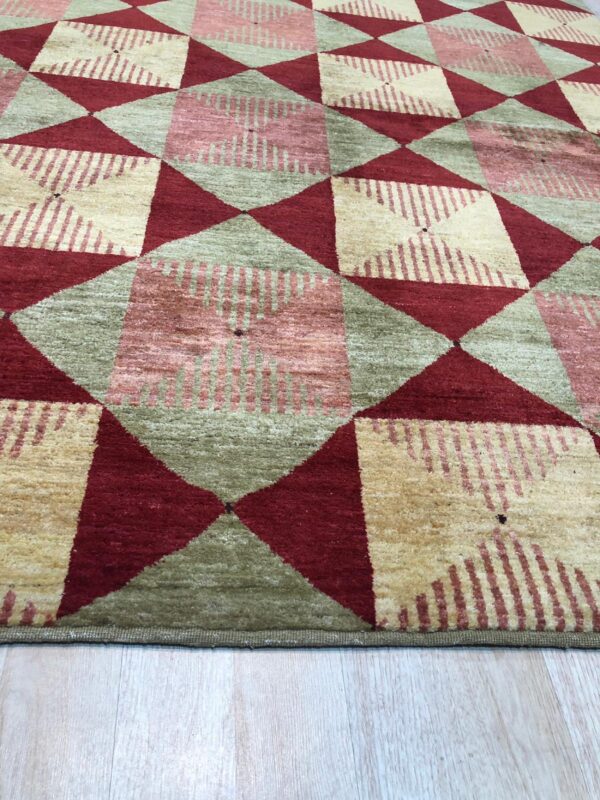 Diamond pattern rug in burgundy, sage green, and striped cream sits on light wood planks.