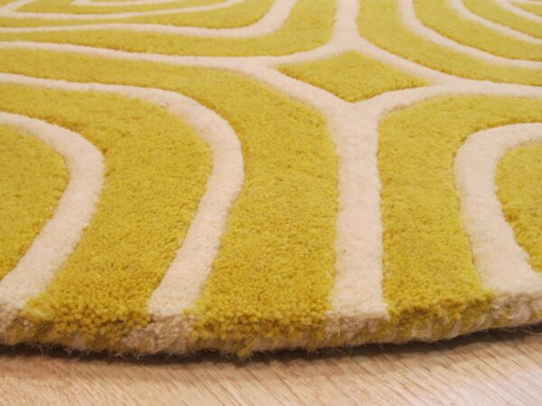 Close-up of a high-pile rug with a curving yellow-green and cream geometric pattern resting on wood flooring.