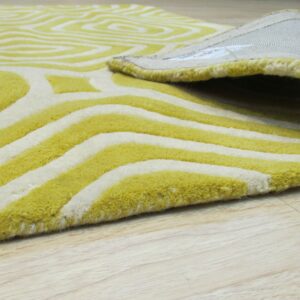 Close-up of a thick, yellow-green and white rug with an abstract geometric pattern laid on light wood flooring.
