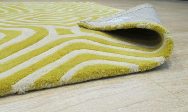 Close-up of a thick, yellow-green and white rug with an abstract geometric pattern laid on light wood flooring.