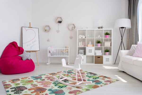 A multicolored elephant pattern rug on a light wood floor anchors a bright white nursery setting.