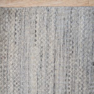 Textural gray and cream area rug featuring segmented vertical stripes rests on light blonde wood flooring.