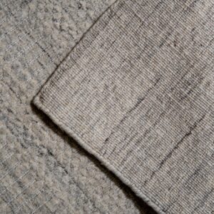 Textured gray rug pile and woven backing are visible in a corner detail shot on light wood planks.
