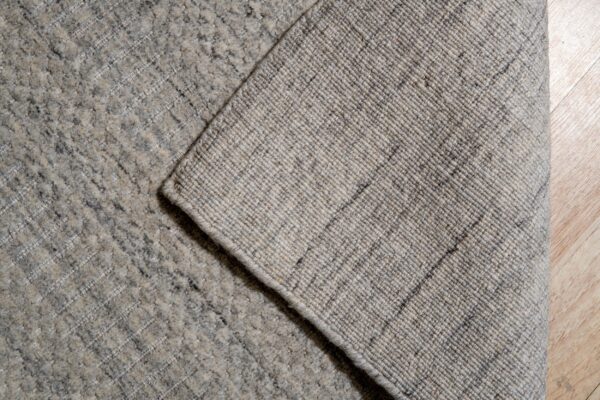 Textured gray rug pile and woven backing are visible in a corner detail shot on light wood planks.
