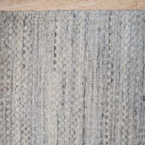 Speckled gray high-pile rug with alternating flat-woven vertical stripes rests on light wood flooring.