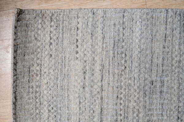Speckled gray high-pile rug with alternating flat-woven vertical stripes rests on light wood flooring.