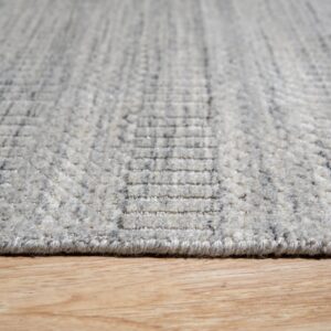 Close-up shows a heathered gray rug with a textured geometric pattern resting on light wood flooring.