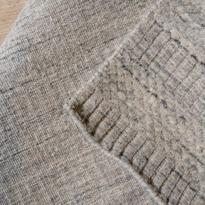 A rolled, heathered gray rug shows its low-pile side and high-pile side with a raised diamond grid pattern.