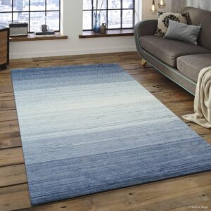 Blue and white horizontal gradient rug lying on distressed wood floors in a room with large windows.