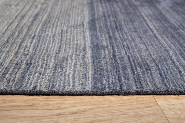 Textured blue rug with vertical cream striations viewed closely against light brown wood flooring.