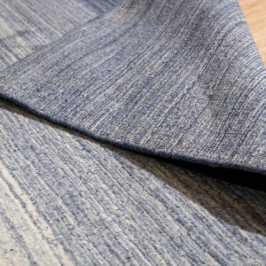 A blue and cream striated rug is partially rolled back on a light wood floor.