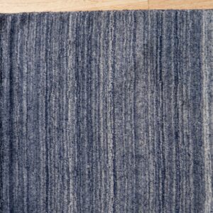 Medium-pile rug with vertical blue and gray faded stripes rests on light wood floor.