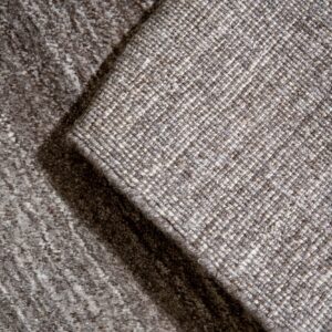 Detail of two neutral rugs overlapping, showing a diagonal woven pattern next to a darker mottled texture.
