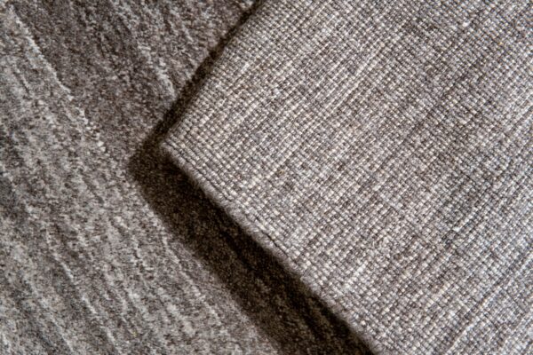 Detail of two neutral rugs overlapping, showing a diagonal woven pattern next to a darker mottled texture.