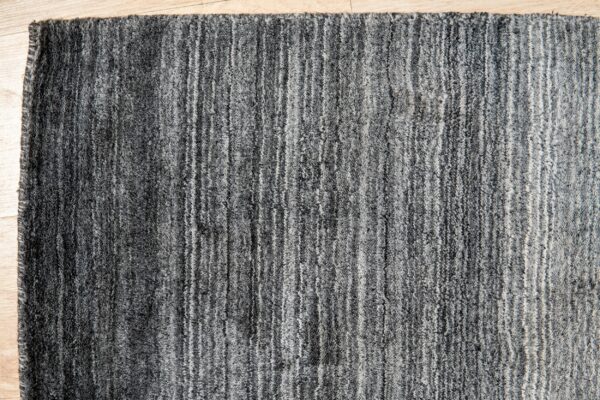 Close-up of a textured dark gray rug with uneven vertical stripes placed on light wood flooring.