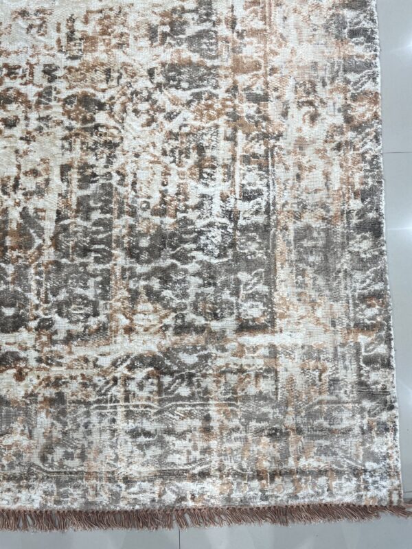 Distressed low-pile rug in cream, gray, and brown with short tassels rests on white tiled flooring.