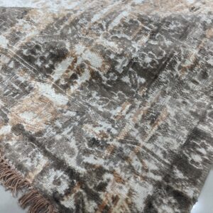 Textured high-low rug featuring an abstract distressed design in brown, white, and tan, with visible fringe on tiled floor.