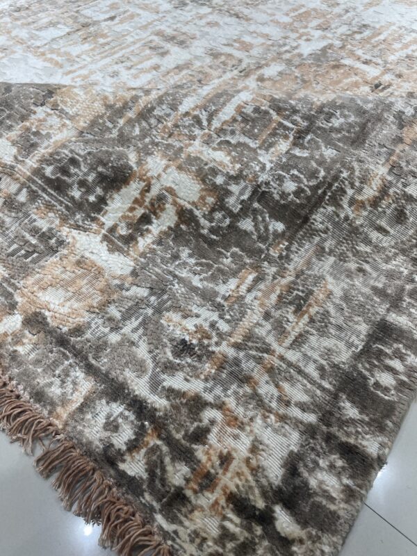 Textured high-low rug featuring an abstract distressed design in brown, white, and tan, with visible fringe on tiled floor.