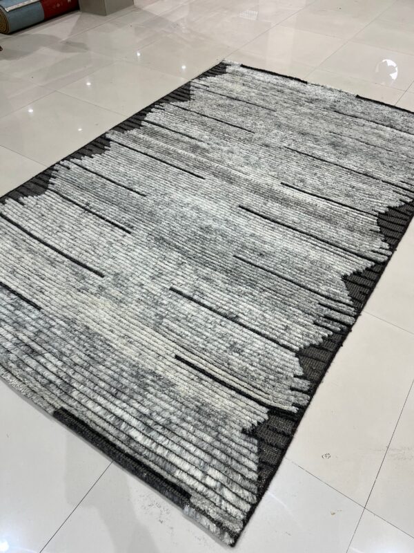 High-pile gray and white rug featuring thick horizontal lines and dark black abstract borders on tile.