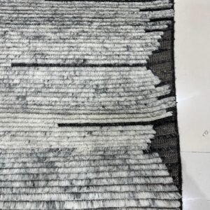High-pile gray and white ribbed rug featuring black stripes and a dark zigzagging edge on white tile.