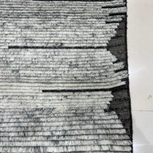 Textured gray and white rug showing thick horizontal stripes and a geometric jagged edge design on tile.