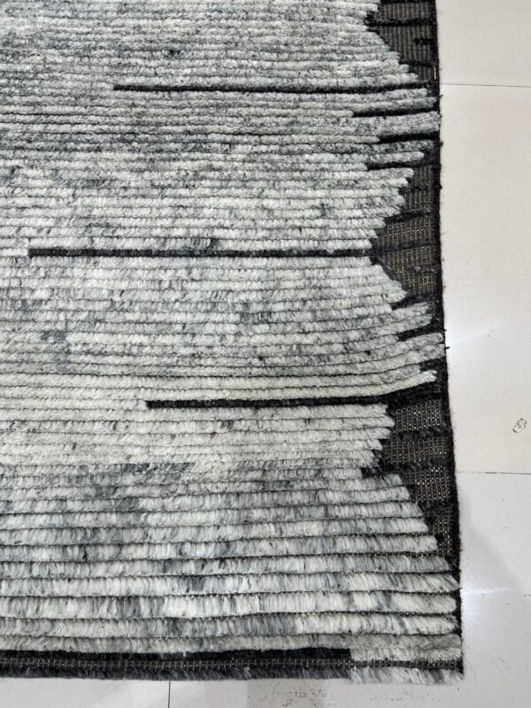 Textured gray and white rug showing thick horizontal stripes and a geometric jagged edge design on tile.