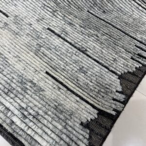 Close-up of a high-pile gray and white rug featuring thick textured ridges and thin black accent lines on white tile.